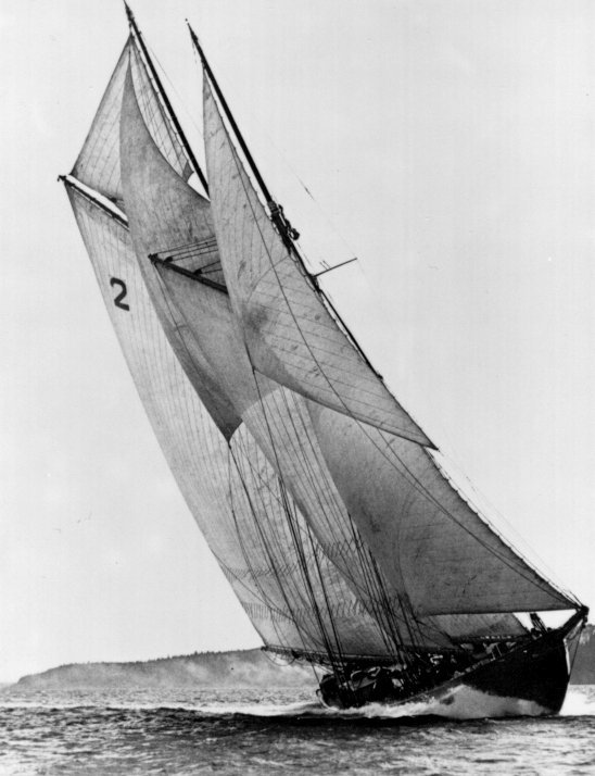 Black and white carved linocut-style print of a large sailboat with full sails leaning over open water near a distant shoreline, rendered in muted grays and deep charcoal tones with a quiet, contemplative mood